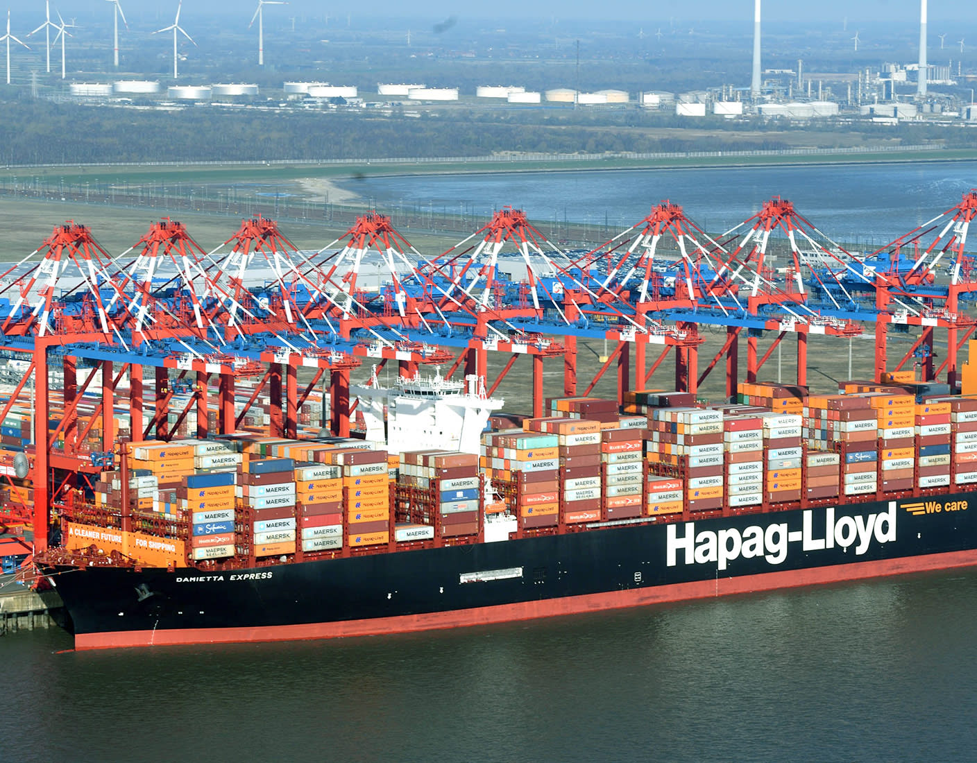 A large Hapag-Lloyd container ship loaded with colorful containers is docked at the port.